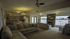 A spacious living room with a large sectional sofa, a fireplace, and a view of a lake. - Waterfront property 25 min from Waterton (Hill Spring)