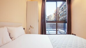 Een hotelkamer met een bed, een bureaulamp en uitzicht op de stad door een groot raam.