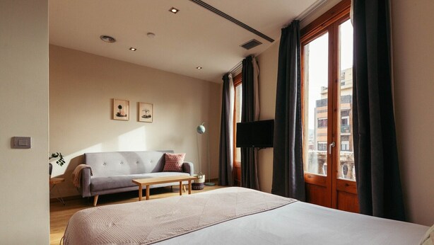 Een slaapkamer met een bed, een bank, een televisie en een raam met gordijnen.
