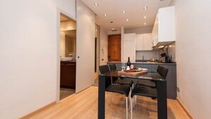 Een moderne keuken met witte kasten, een houten deur en een eethoek met een glazen tafel en zwarte stoelen.