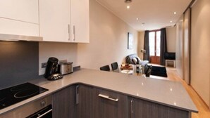 Een moderne keuken met een ingebouwde kookplaat, een eethoek met tafel en stoelen, en zicht op de woonkamer.