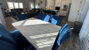 Une cuisine moderne avec des meubles blancs, un îlot central et un coin repas agrémenté de chaises bleues et d’une table en marbre.