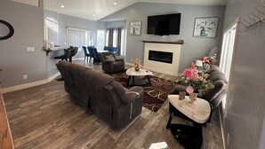 Un salon spacieux avec un canapé gris, une table basse et une cheminée. On aperçoit à l’arrière-plan un coin repas avec une table et des chaises.