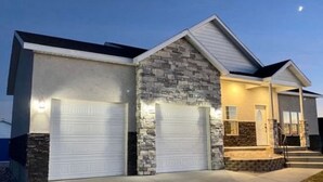 Une maison moderne à deux étages, dotée d’une façade en pierre et de deux portes de garage.