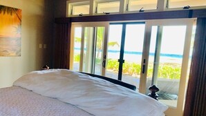 A bedroom with a large bed, a view of the beach through sliding glass doors, and a painting on the wall. - Spend some time on Puako Beach. (Waimea)