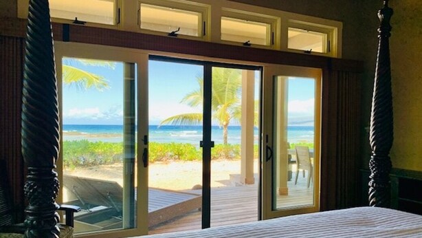 A bedroom with a large bed, a sliding glass door leading to a beach view, and a wooden ceiling. - Spend some time on Puako Beach. (Waimea)