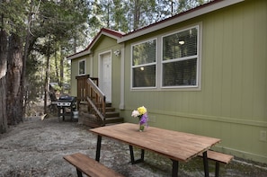 A small, single-story building with a green exterior and white trim. It features a front door, a set of stairs leading to a porch, and a wooden table with benches. - (3R) Suter's Forte at The Redwoods In Yosemite (Yosemite National Park)
