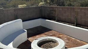 Un jardín en la azotea con una jardinera de hormigón, un pequeño hogar para fuego y vistas al paisaje desértico con cactus.