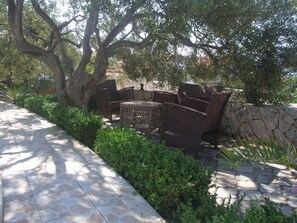 Relax in a serene outdoor space surrounded by lush greenery and a stone wall, with a wicker seating area.