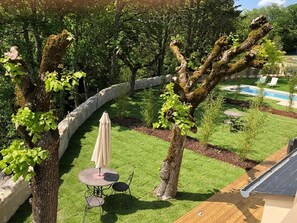 Relax in a serene outdoor space surrounded by lush greenery, featuring a lawn, a wooden deck, and a swimming pool.