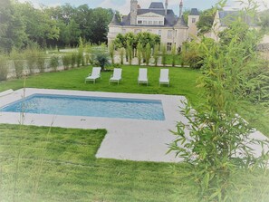 Relax by the serene pool surrounded by lush greenery and a stately building with a classic design.