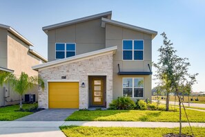 A modern two-story house with a stone facade, a yellow garage door, and a well-maintained lawn. - Exquisite 5BR Retreat with Pool - Champions Gate - 871 (Davenport)
