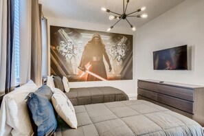 Ett sovrum med en stor väggmålning med Star Wars-tema, en modern säng, en tv och en modern taklampa.