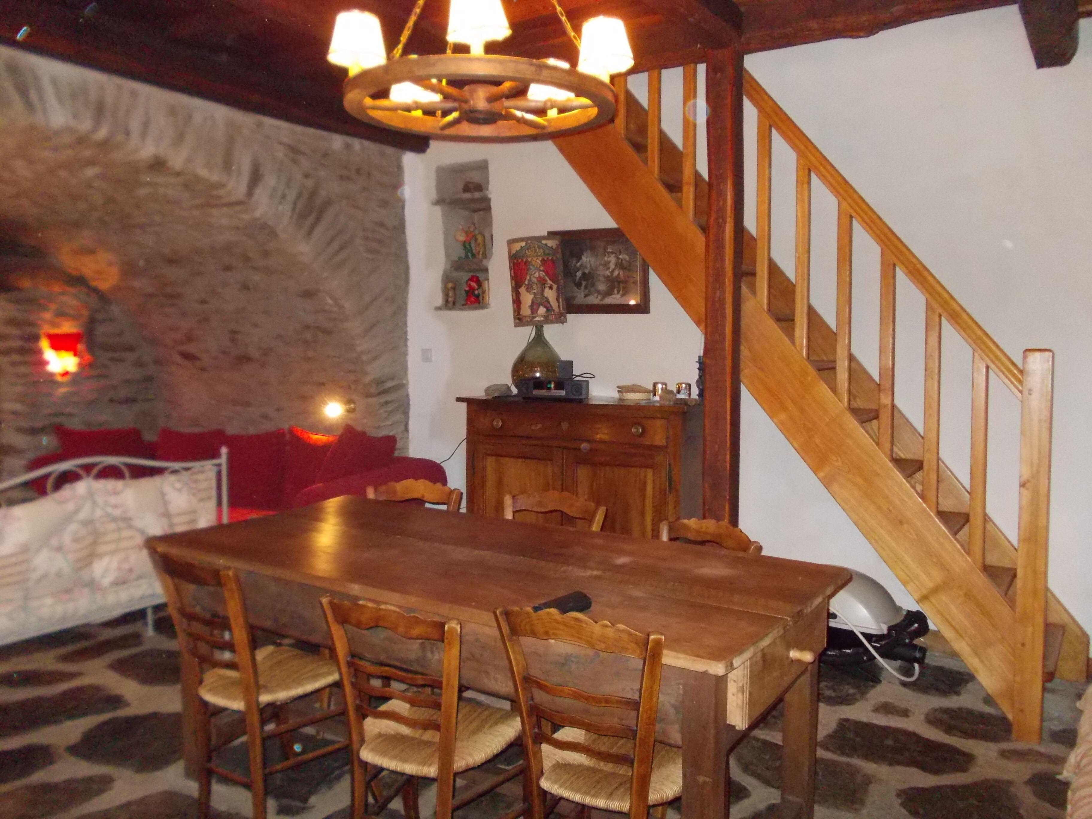 A dining area with a wooden table and chairs, a staircase, and a stone wall.