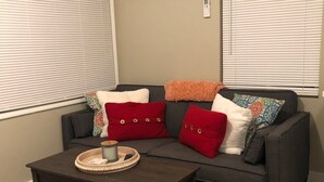 Ein Wohnzimmer mit einem dunkelbraunen Couchtisch, einem grauen Sofa mit roten und weißen Kissen sowie einem beigen Teppich.