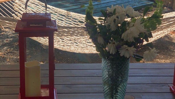 Eine Holzterrasse mit einer Hängematte, einem roten Laternen und einem Blumenstrauß mit weißen Blüten.
