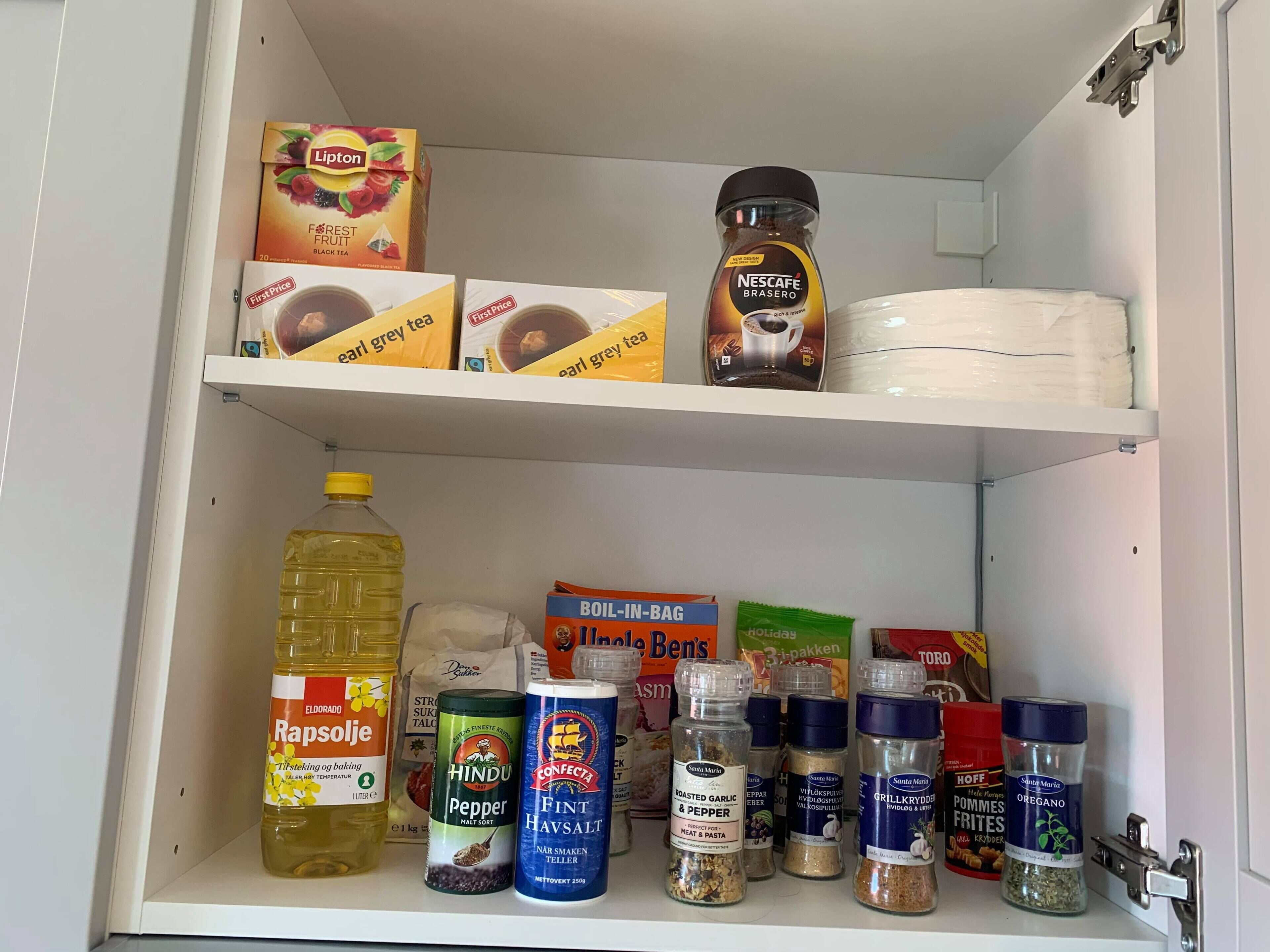 Una despensa con diversos productos alimenticios, incluyendo frascos de especias, una botella de Rapsolje y cajas de té.