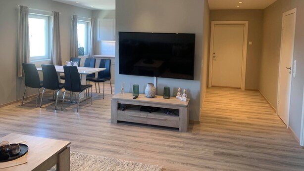 A modern living room with a flat-screen TV, a dining area with chairs, and a wooden floor. - Notodden Sentrum Apartment NO 6 (Notodden)