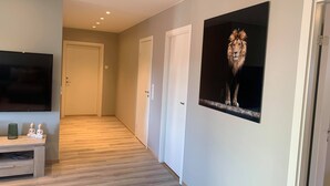 A hallway with a wooden floor, a flat-screen TV on the left, and a framed picture of a lion on the right. - Notodden Sentrum Apartment NO 6 (Notodden)