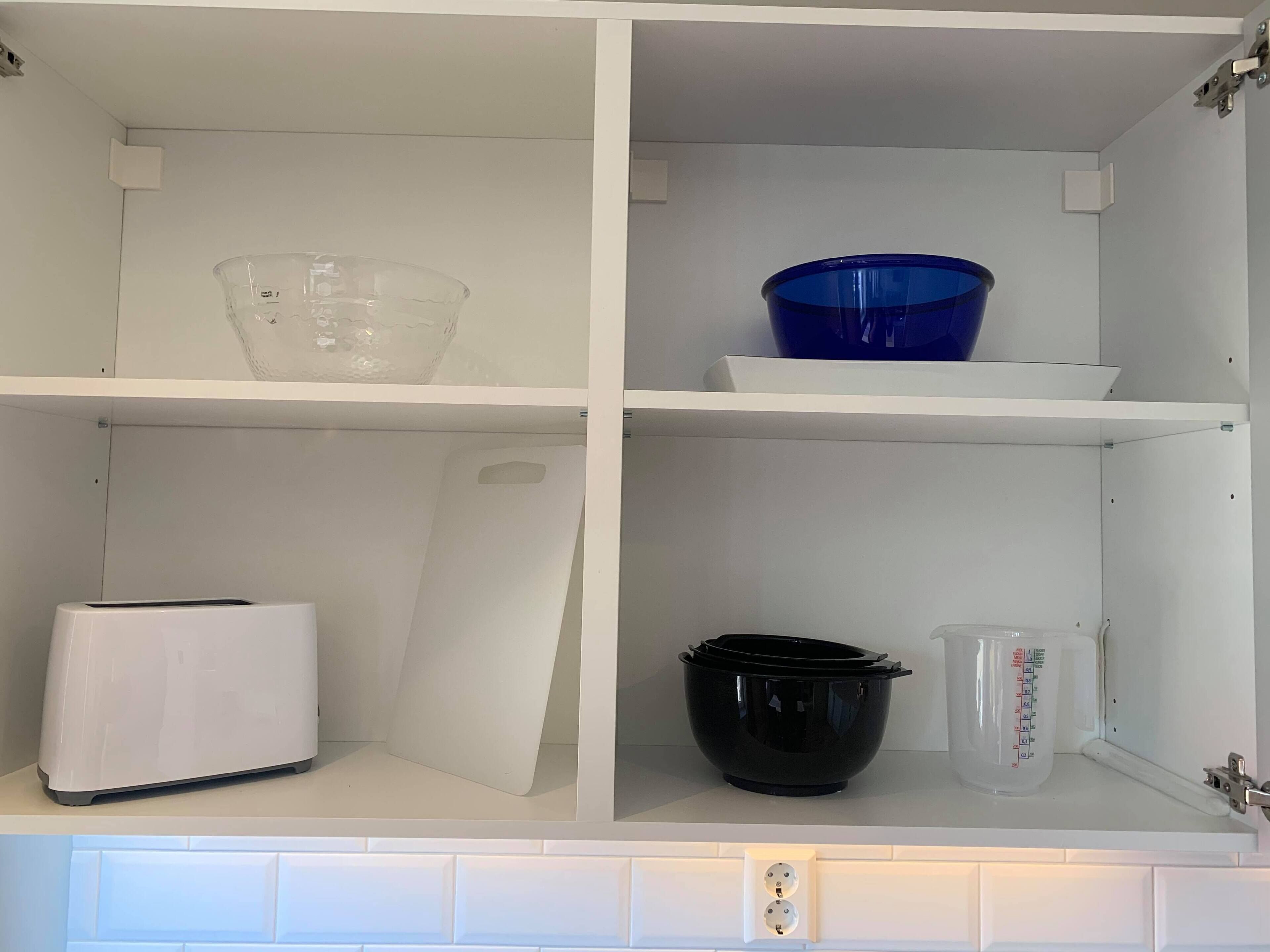 Un armario de cocina con estantes que contienen un vaso medidor, una olla negra y una tostadora blanca.
