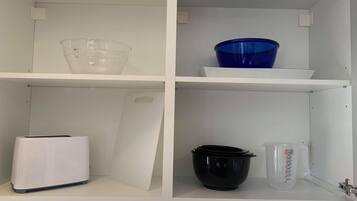 Un armario de cocina con estantes que contienen un vaso medidor, una olla negra y una tostadora blanca.