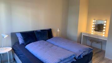 A neatly made bed with a blue patterned duvet, a bedside lamp, and a vanity with a mirror and lights.
