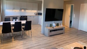 A modern kitchen with white cabinets, a dining area with a table and chairs, and a flat-screen TV mounted on a wall. - Notodden Sentrum Apartment NO 6 (Notodden)