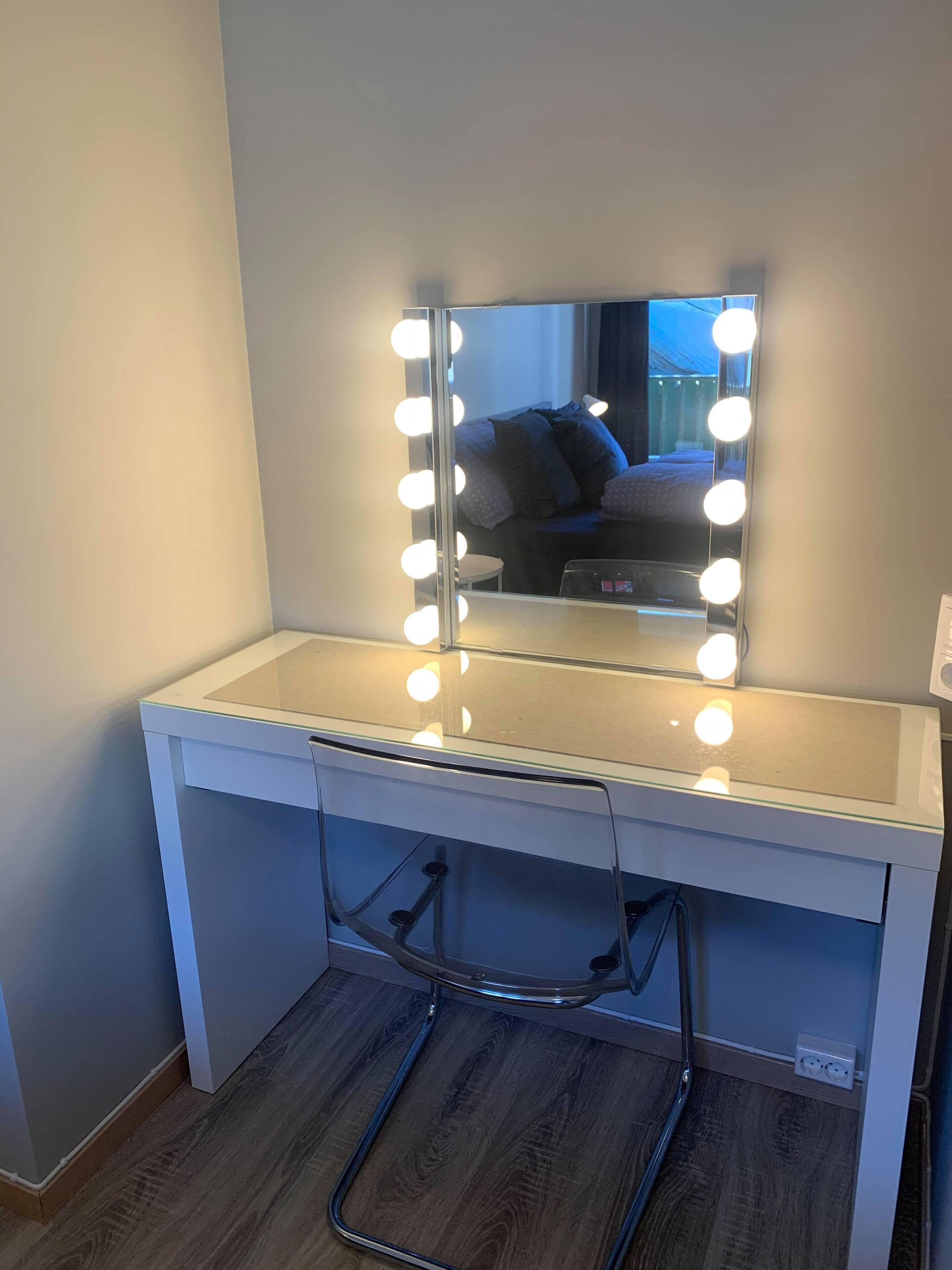 A vanity with a mirror and lights, a white countertop, and a wooden floor.