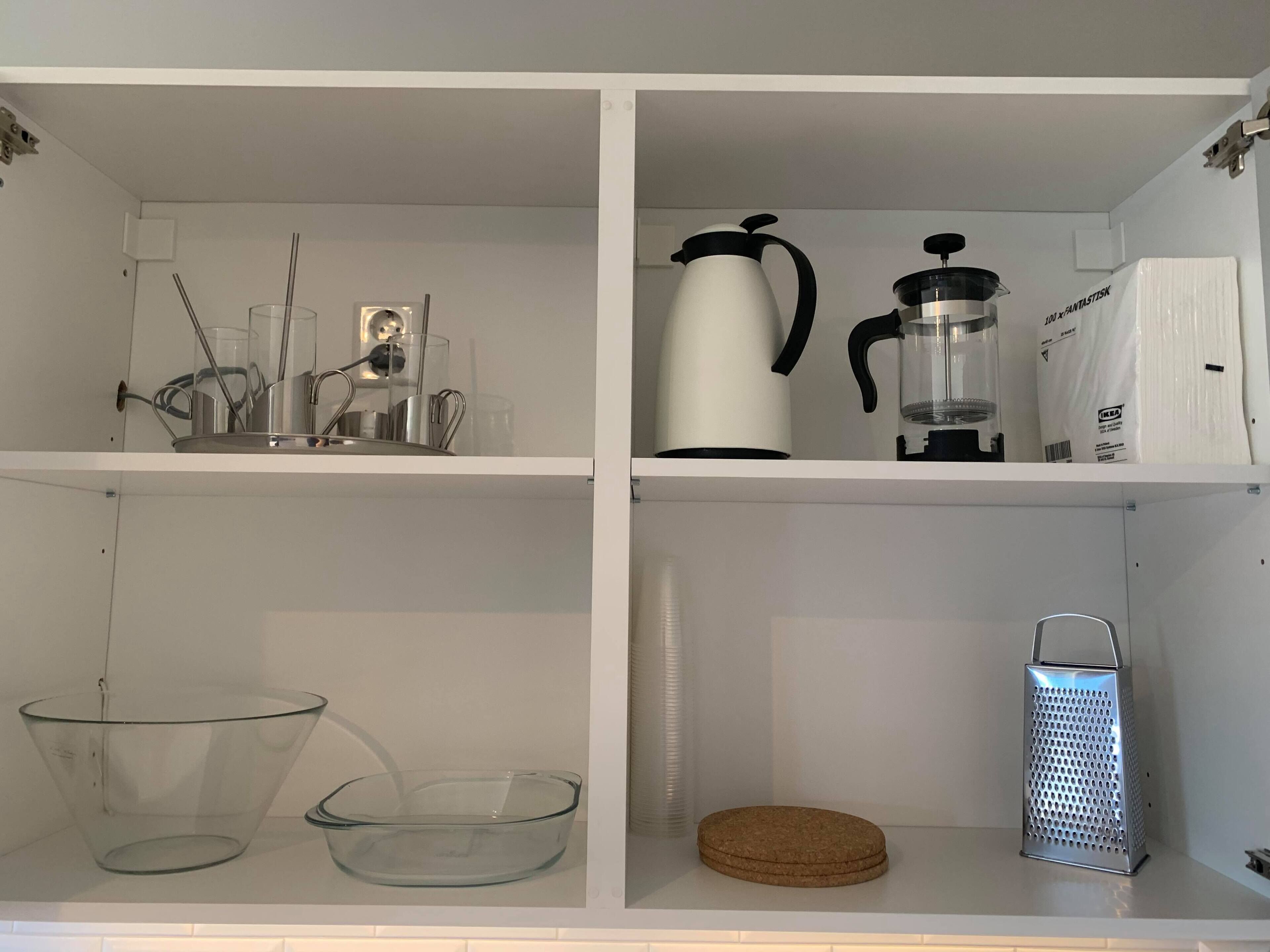 A kitchen with white cabinets, a coffee maker, a kettle, a grater, and a glass container.
