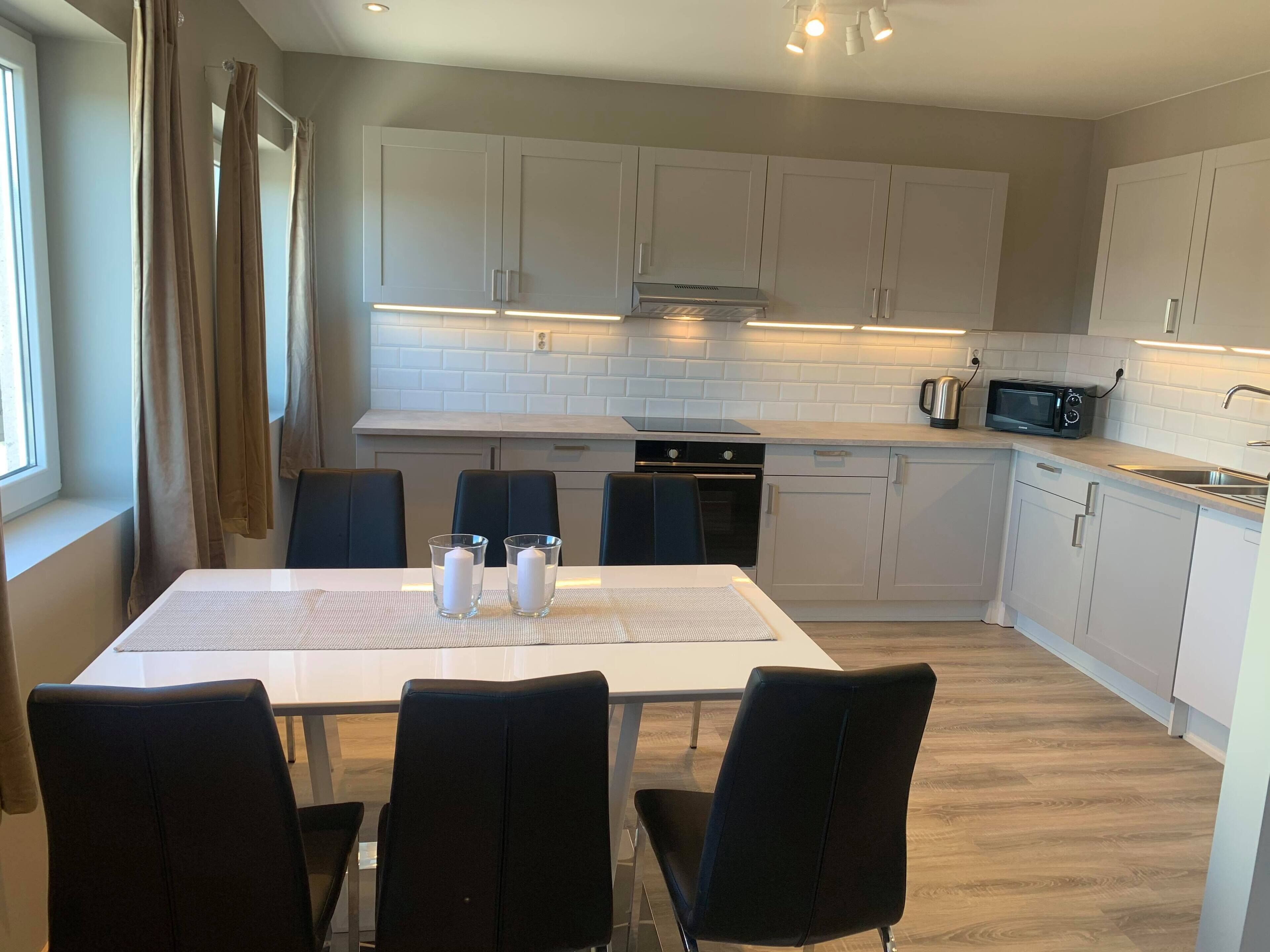 A modern kitchen with white cabinets, a dining table with chairs, and a microwave.