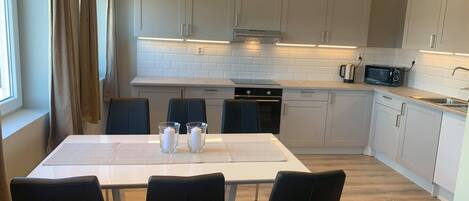 A modern kitchen with white cabinets, a dining table with chairs, and a microwave.