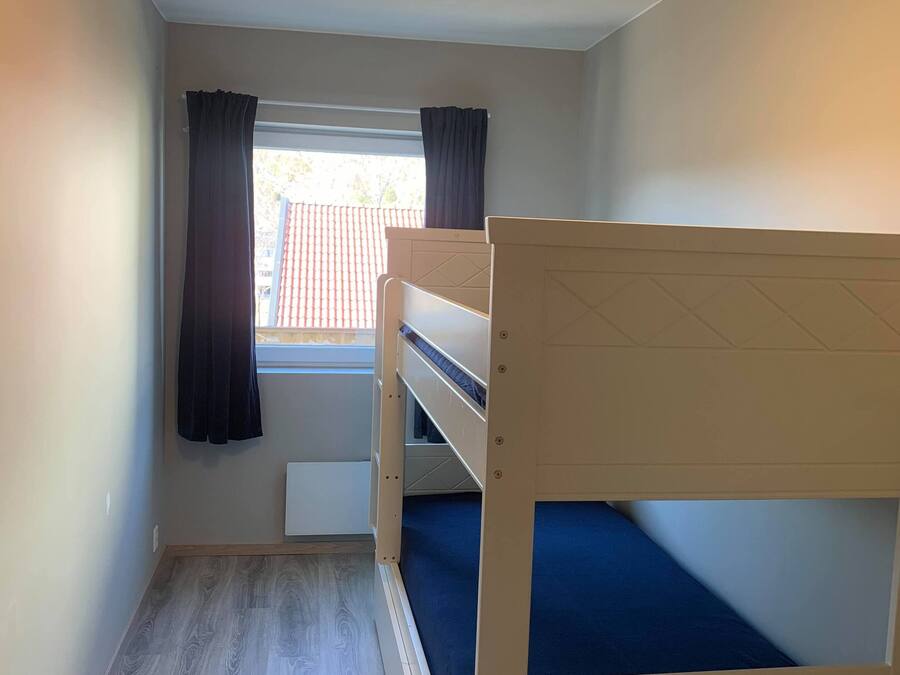 Una habitación pequeña y luminosa con literas, una ventana con cortinas y un radiador.