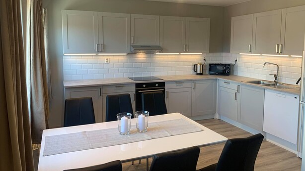 Una cocina moderna con armarios blancos, microondas integrado, pileta de acero inoxidable y un comedor con mesa y sillas.