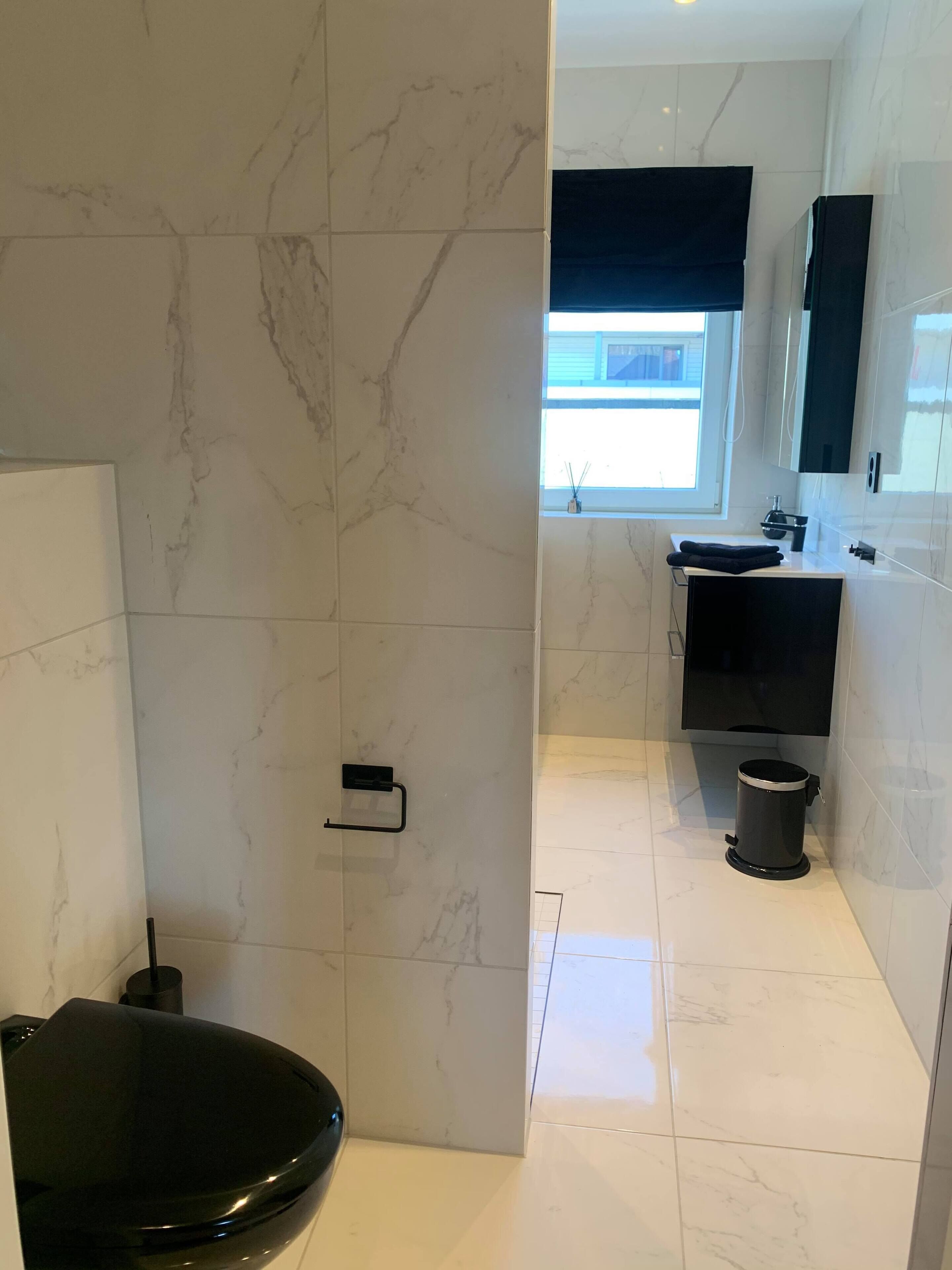 Une salle de bain moderne avec un lavabo noir, des carreaux de marbre blanc et un grand miroir.