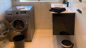 A compact hotel bathroom with a washing machine, a sink, a mirror, and a window with a view of the street. - Notodden Sentrum Apartment NO 6 (Notodden)