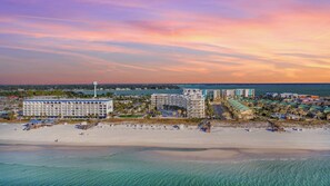 Un hôtel en bord de mer composé de plusieurs bâtiments, doté d’une plage avec des parasols et offrant une vue dégagée sur l’océan.