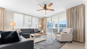A modern living room with a sofa, armchair, and coffee table. There is a ceiling fan and large windows with blinds. - Destin West Osprey 506 ~ Breathtaking Bay Views ~ Lazy River (Fort Walton Beach)