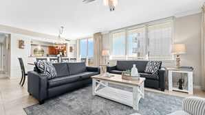 A modern living room with a black sectional sofa, a wooden coffee table, and a striped armchair. There is a dining area with a chandelier and a kitchen in the background. - Destin West Osprey 506 ~ Breathtaking Bay Views ~ Lazy River (Fort Walton Beach)