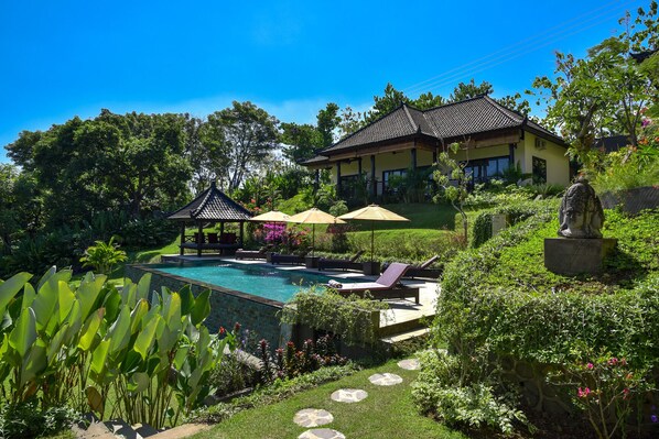 A pool area with lounge chairs, umbrellas, and a gazebo.