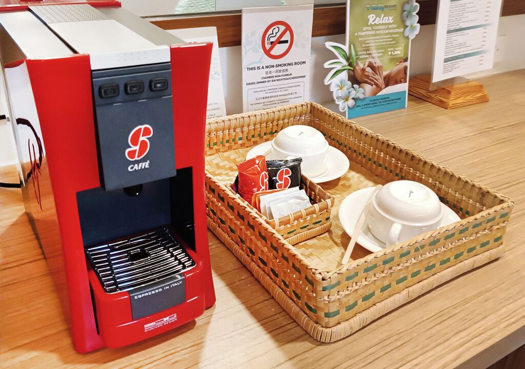 Una máquina de espresso roja y negra con una canasta que contiene dos tazas blancas y un paquete rojo.