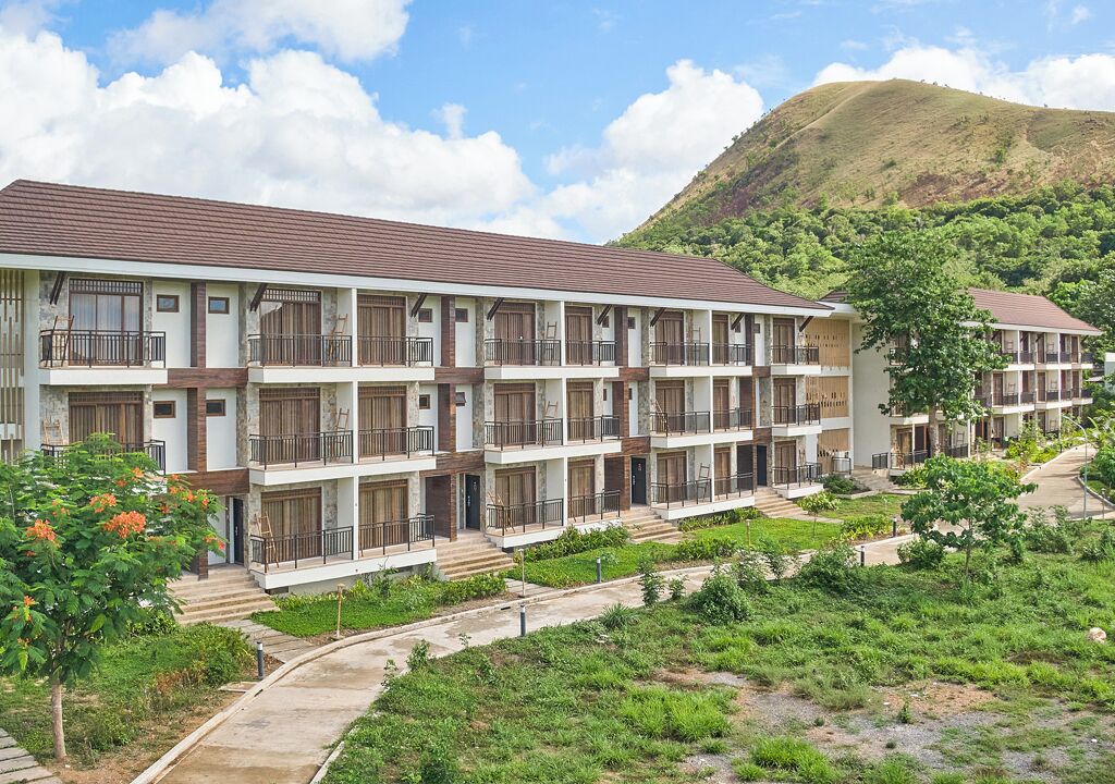 Un hôtel à plusieurs étages doté de balcons, situé au pied d’une colline et agrémenté d’un jardin aménagé.