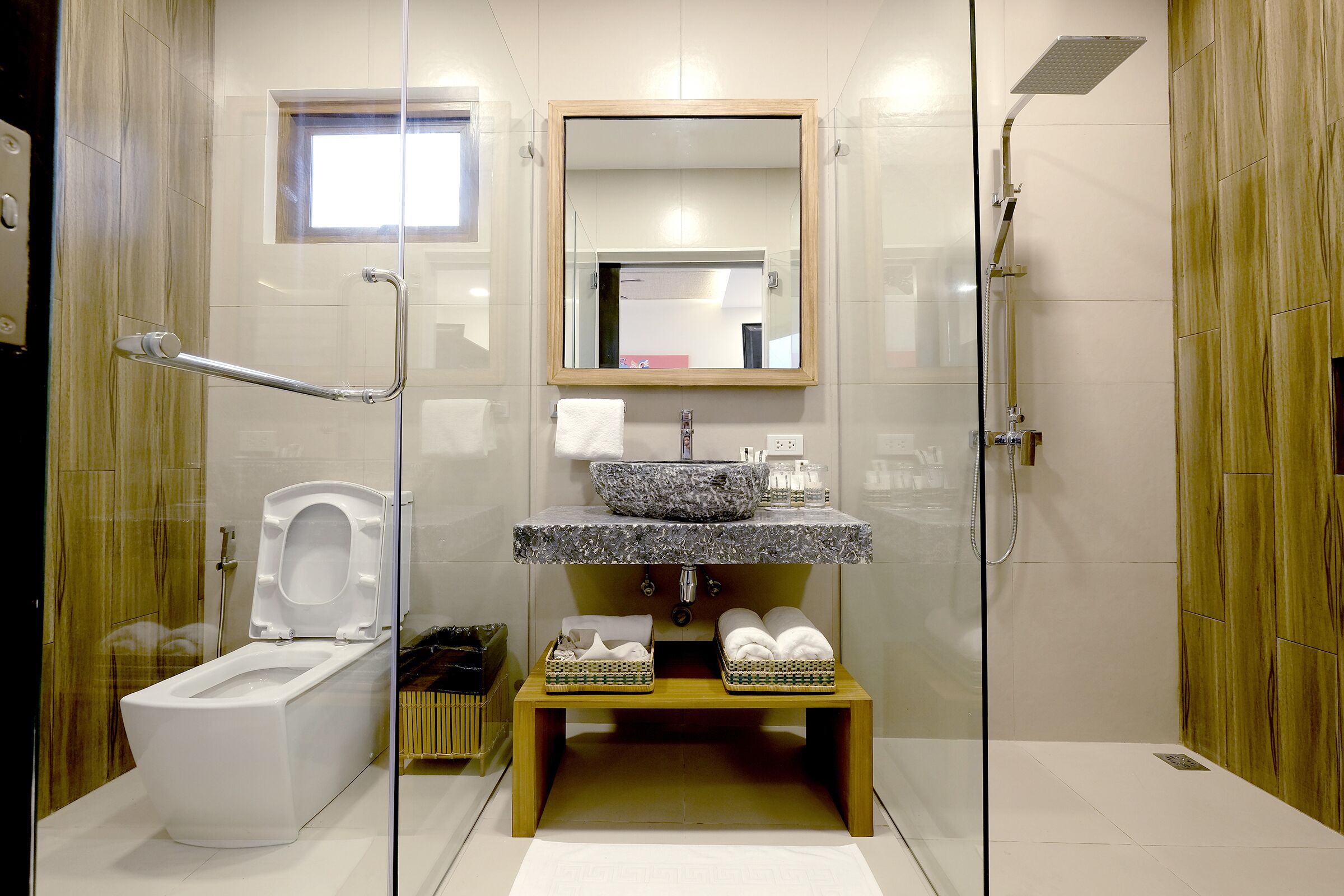 A modern bathroom with a glass-enclosed shower, a toilet, and a vanity with a granite countertop and a mirror above it.