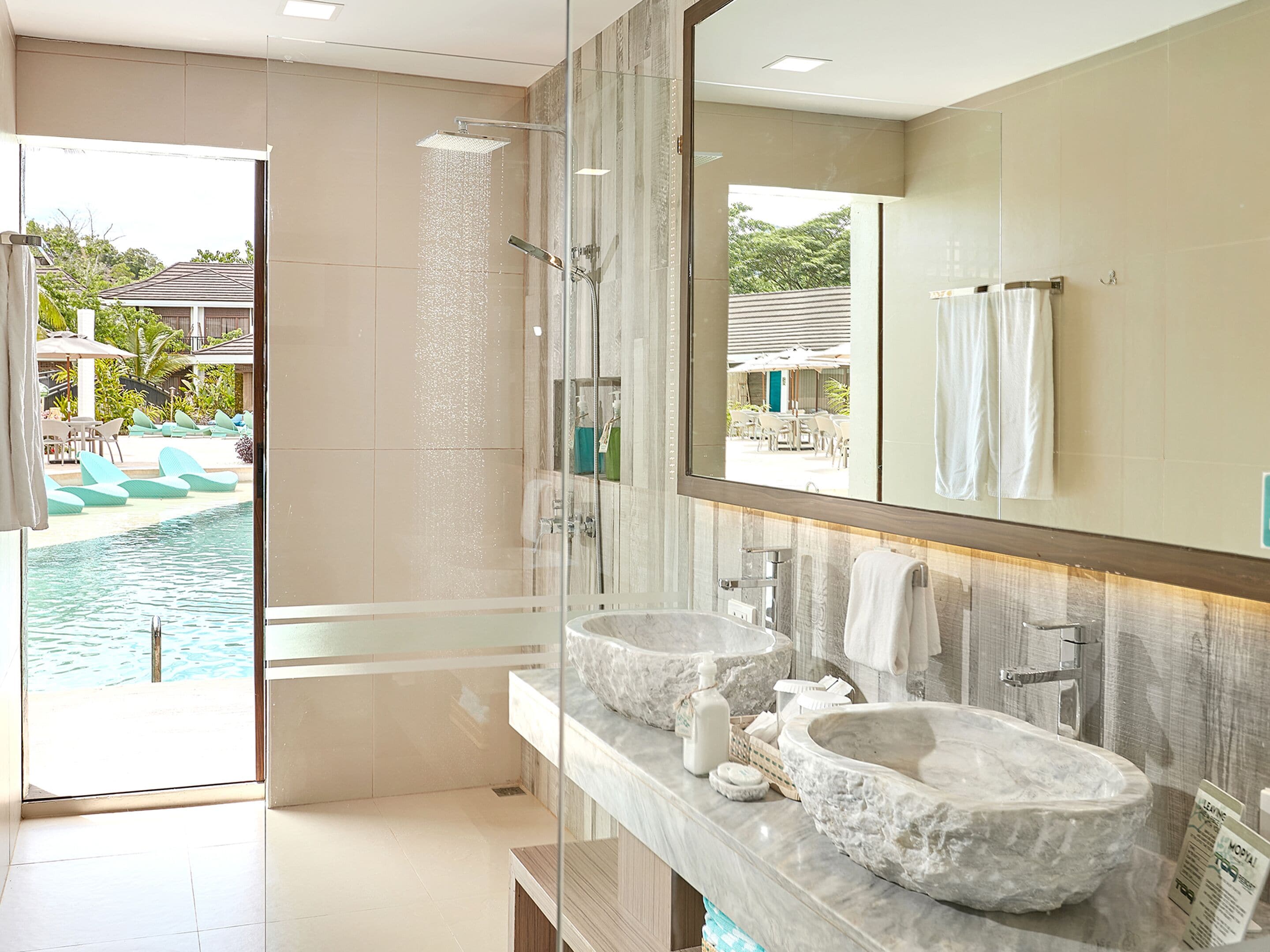 Un baño moderno con cabina de ducha de vidrio, un espejo grande y dos lavamanos de piedra.