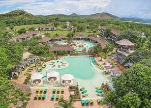 A resort with a large swimming pool, multiple guest rooms, and lush greenery.