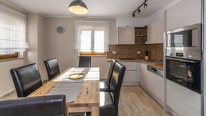 Een moderne keuken met een houten eettafel, zwarte stoelen en inbouwapparatuur, waaronder een magnetron en oven.