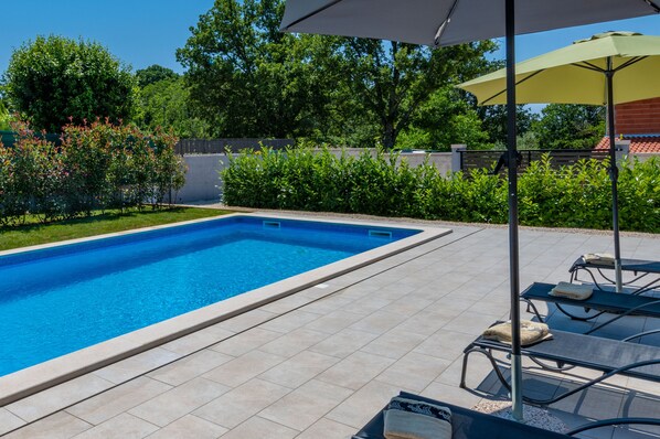 A rectangular swimming pool with tiled edges, surrounded by a patio area with lounge chairs and a yellow umbrella. - Günstig Gelegene Neubau-villa mit Pool (Poreč)