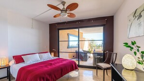 Une chambre moderne avec un lit, un ventilateur de plafond, une grande fenêtre et une vue sur l’extérieur.
