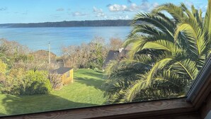 Blick aus einem Fenster auf ein Gewässer, mit blauem Himmel und vereinzelten Wolken.