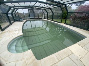 A covered swimming pool with a glass enclosure, surrounded by a patio area with outdoor furniture. - A haven of peace overlooking the sea (Plestin-les-Grèves)