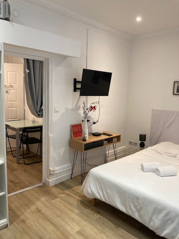 Une chambre d’hôtel comprenant un lit, un bureau avec une chaise, un téléviseur fixé au mur et une petite table avec un vase et un panneau.